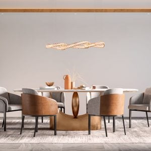 Uma sala de jantar vista de frente, um tapete cinza no chão e acima uma mesa redonda com 6 cadeiras. O conjunto possui detalhes em dourado, marrom e cinza e em cima da mesa possui alguns objetos como um vazo de planta, uma garrafa térmica de café, um bowl dourado e alguns livros. Acima da mesa há o Pendente led LEZIE ORI iluminando o ambiente.