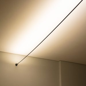 A imagem exibe o Kit Luminária SKYLINE, um sistema de iluminação que utiliza fita LED para criar uma iluminação indireta elegante no teto ou parede. O material de alumínio proporciona um visual moderno e é resistente. Na fotografia, podemos ver a luz suave emanando do perfil de alumínio, realçando a textura da superfície e contribuindo para uma atmosfera acolhedora. Disponível em medidas de 5 metros ou 10 metros, adapta-se a diferentes tamanhos de espaços, seja em residências ou ambientes comerciais.