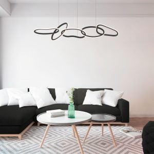 A imagem mostra o pendente led ZENA da Nordecor, destacando-se no espaço acima de um sofá preto com almofadas brancas, complementando o ambiente com um design moderno e uma iluminação aconchegante.