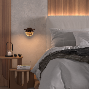 Modern bedroom scene with an upholstered gray bed, warm wall lighting, and a round wooden nightstand holding a lantern and books.