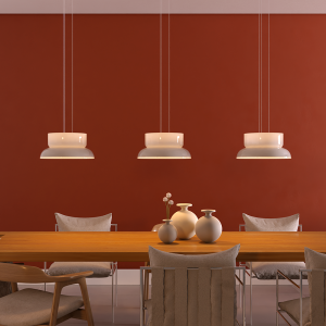 Three white pendant lamps hang over a wooden dining table in a red-walled room with minimalist vases and chairs around the table, creating a warm dining setting,